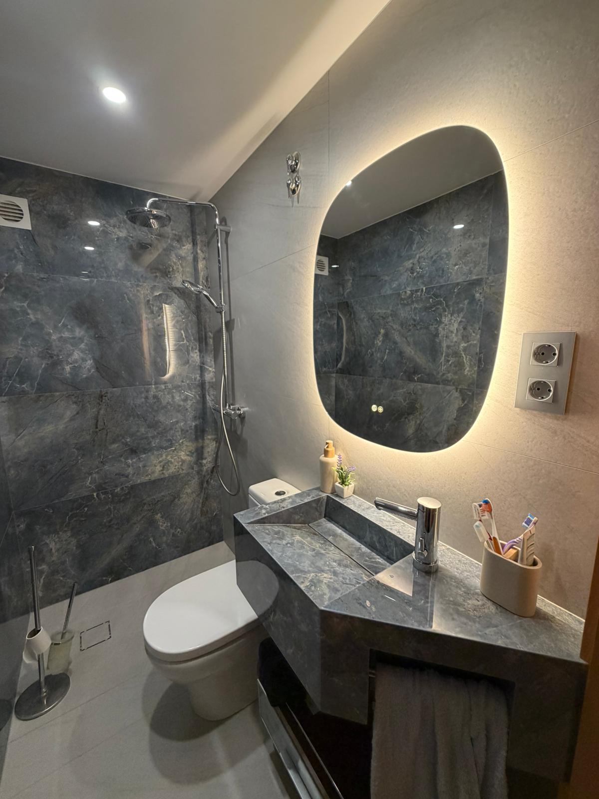 Encimera veteada oscura con lavabo integrado y espejo iluminado